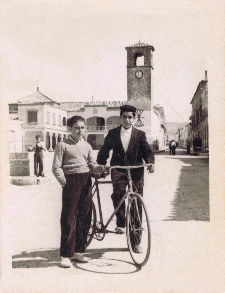 Eutimio Zarco Zarco, a la izquierda, y Román Tinajero Moreno, en la plaza de Mota del Cuervo, allá por el año 1956. Al fondo, el ayuntamiento, y lo que se ve detrás de ellos, donde está el chicote, es parte de la fuente hexagonal que había en la plaza en aquella época.